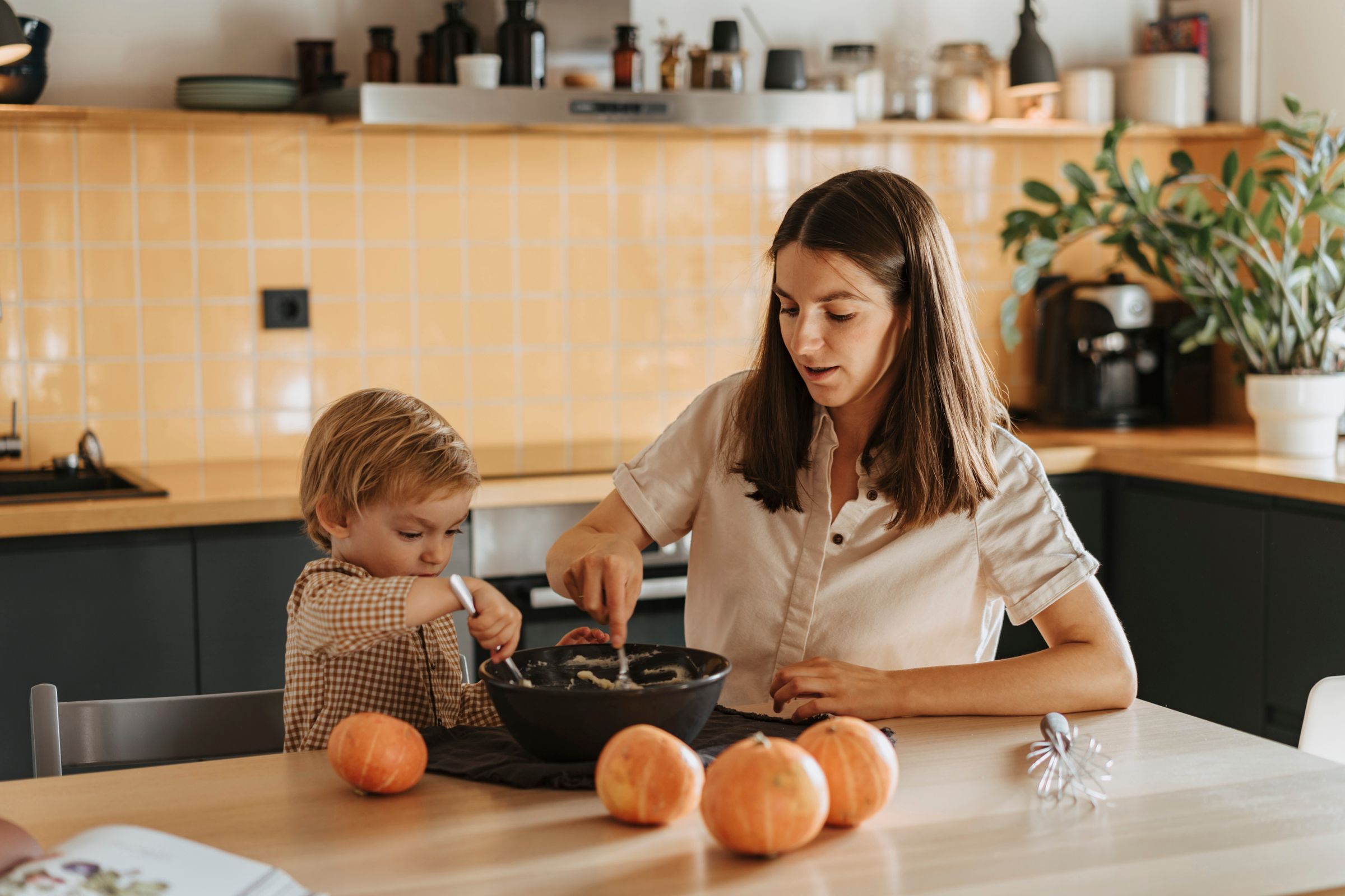 Mother and child cooking together in a warm modern kitchen decorated with pumpkins for fall